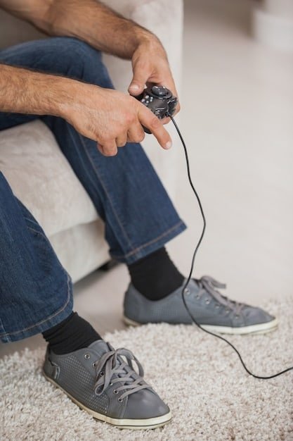 A person with limited mobility using the Xbox Adaptive Controller with their feet. Multiple assistive switches and joysticks are connected to the controller. The person is smiling as they play a racing game on a large monitor in front of them.